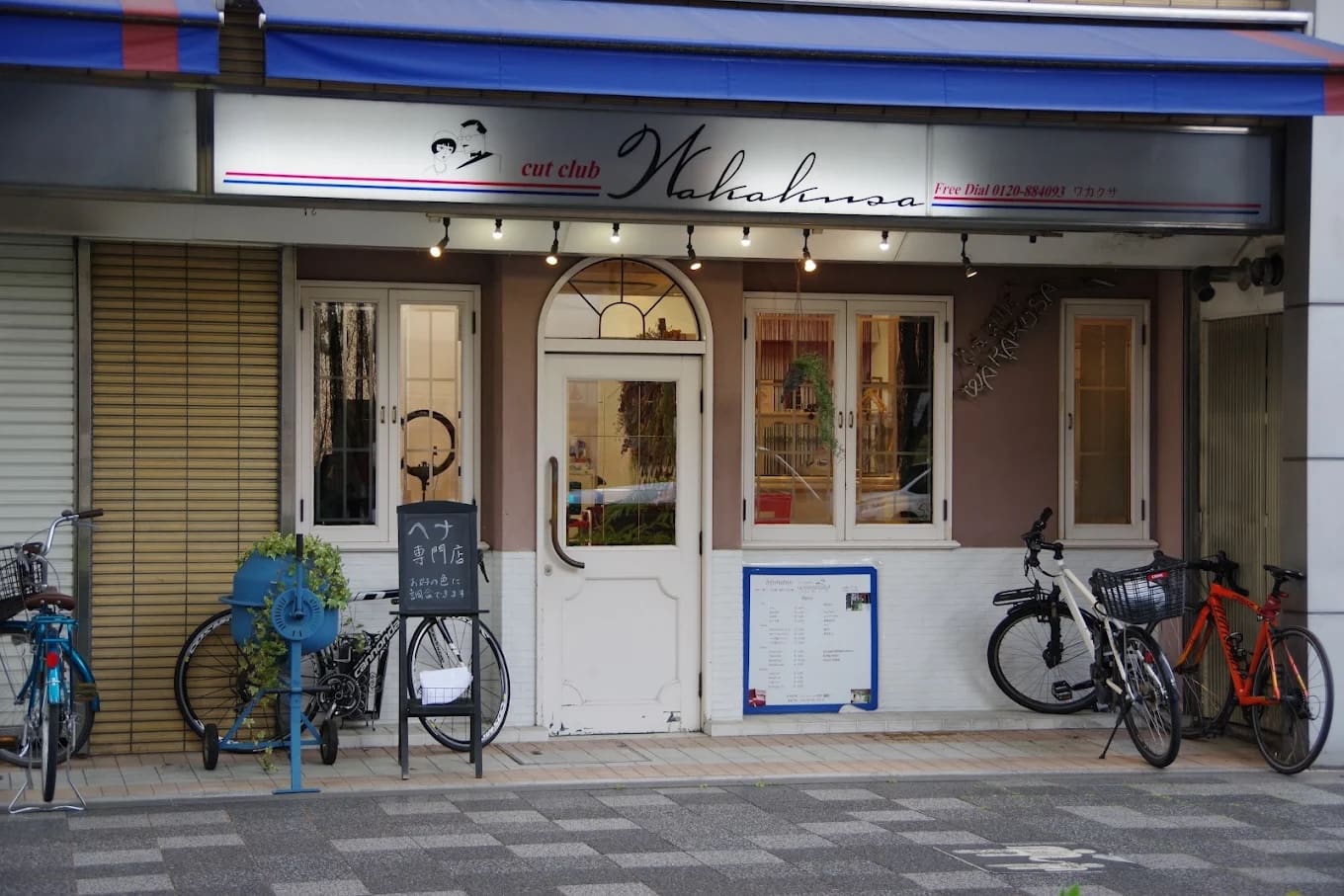 ร้านมีป้ายเขียนว่า "คัทคลับวาคานะ" ที่ด้านบนของประตูสองบานสีขาว และให้บริการทางลัดและเฮนน่า คั่นกลางระหว่างหน้าต่างและลานจอดจักรยาน มีชั้นวางจักรยานสีน้ําเงิน กระถางต้นไม้ เมนูและป้ายใกล้ทางเข้า