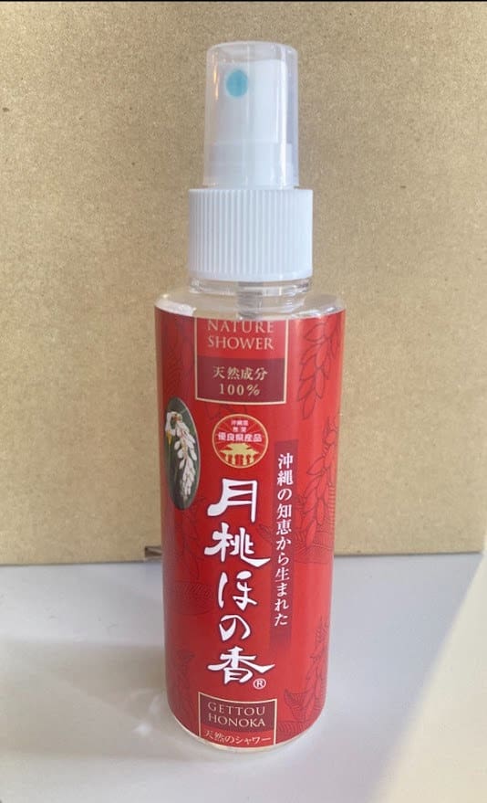 ขวดสเปรย์สีแดงที่มีคําว่า "Nature Shower" เขียนบนพื้นหลังสีเบจ หัวฉีดสเปรย์สีขาวและฝาปิด