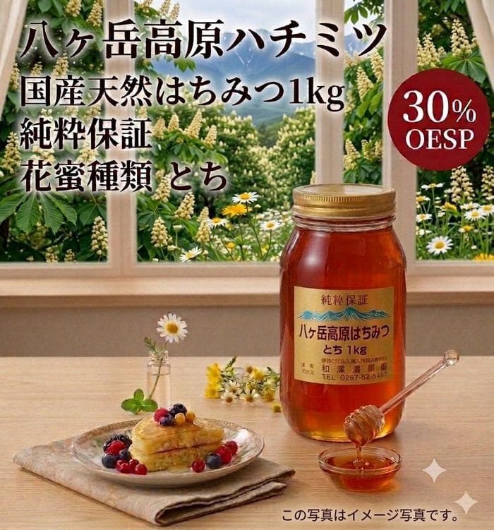 「八ヶ岳高原 国産天然はちみつ 1kg 純粋保証（花蜜の種類：トチ）」の瓶とハチミツ用スプーンが、フルーツをトッピングしたパンケーキの乗ったお皿の隣のテーブルに置かれている。背景には花や緑が飾られており、画像には日本語の文字と赤い「30% OESP」のラベルが見える。.